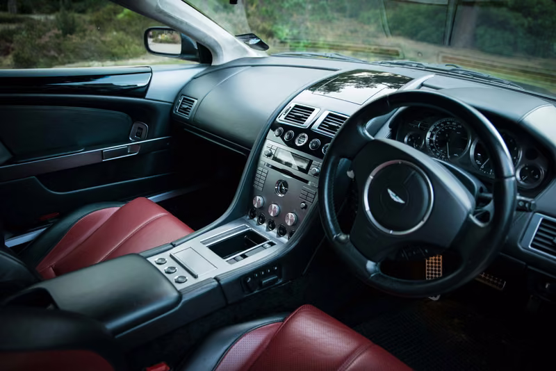 Aston Martin DB9 cockpit with red leather seats, a black dashboard and silver centre console.